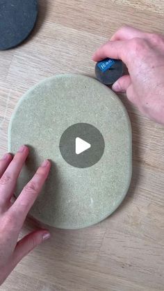 two hands are working on an object that looks like a disk with a video playing button