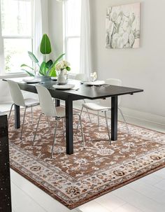 a dining room table with white chairs and a rug on the floor in front of it