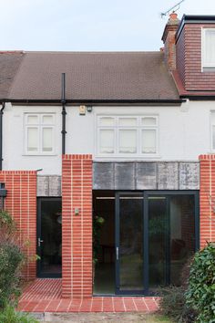 an empty brick building with doors and windows on the outside, in front of some bushes