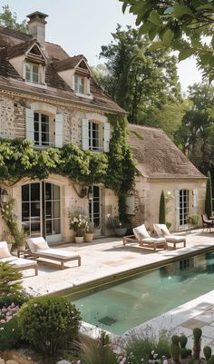 an outdoor swimming pool with chaise lounges in front of a large stone house