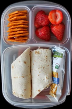 a lunch box with strawberries, crackers, and tortilla wrap in it