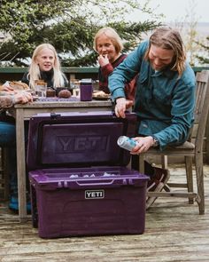 three people sitting at a table with purple coolers