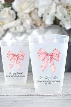 two plastic cups with pink bows on them sitting on a table next to white flowers