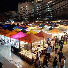 an outdoor market with lots of colorful umbrellas and people walking around it at night