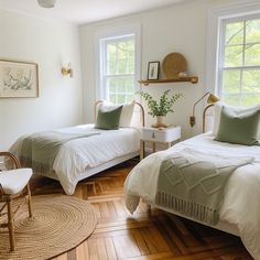 two beds in a bedroom with wooden floors and white walls, one has green pillows on it