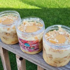 three jars filled with desserts sitting on top of a wooden table next to grass