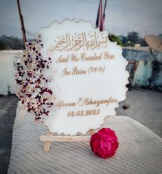 a white sign sitting on top of a bed next to a red rose