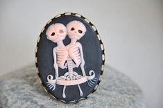 a ring with two skeletons on it sitting on top of a gray rock, in front of a white wall