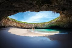 two people are walking on the beach in front of an ocean cave with clear blue water