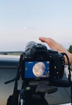 a person holding up a camera to take a photo with the moon in the background