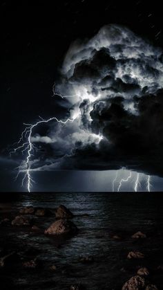 lightning strikes over the ocean and rocks