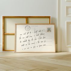 a framed postcard sitting on top of a hard wood floor next to a white wall