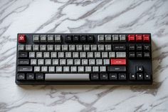 a computer keyboard sitting on top of a white marble countertop covered in red and black keys