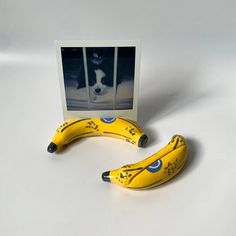 two yellow bananas sitting next to each other on top of a white table with a black and white dog in the background