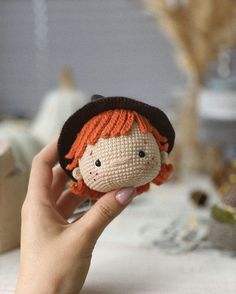 a hand holding a small doll with red hair and a black hat on it's head