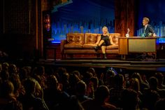 a man and woman sitting on couches in front of an audience at a television show