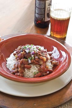 a red plate topped with rice and beans on top of a wooden table next to a beer