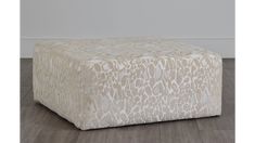 a white and beige ottoman sitting on top of a hard wood floor next to a wall