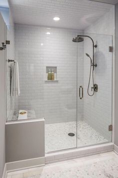 a walk in shower sitting next to a white tiled wall and floor with a glass door