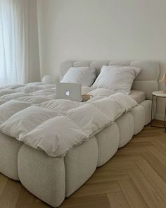 a bed that has a laptop on it in the middle of a room with wood floors