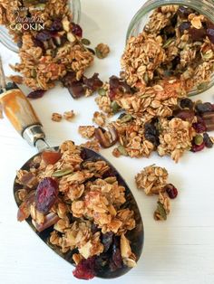 granola in a spoon on top of a white table next to other granola ingredients