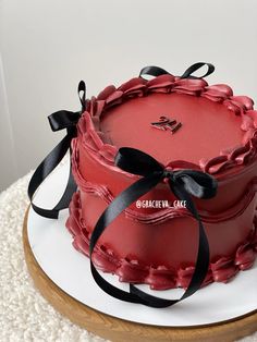 a red cake with black ribbon and bow sitting on top of a white platter