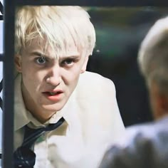 a man with blonde hair wearing a white shirt and tie looking at himself in the mirror