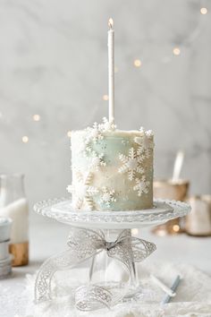 a white frosted cake sitting on top of a glass platter with a lit candle