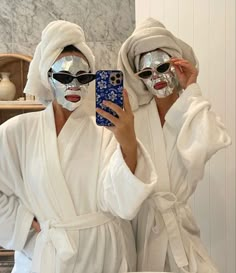 two people in white robes are taking a selfie with their face masks and one is holding a cell phone