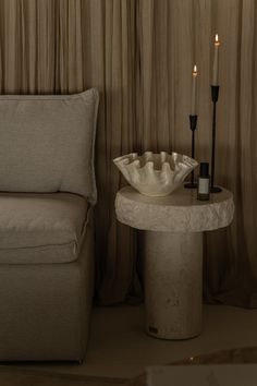 a table with a bowl on it next to a couch and two candles in the background