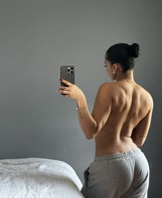 a woman taking a selfie with her cell phone on the bed while wearing grey sweatpants