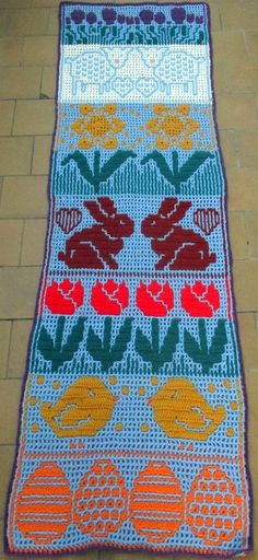 a crocheted rug on the ground with flowers and leaves in red, orange, blue, yellow and green