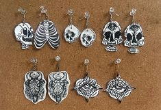 six pairs of earrings with different designs on them sitting on a brown surface next to each other