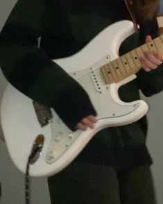 a person holding a white electric guitar in their right hand and wearing a black hoodie