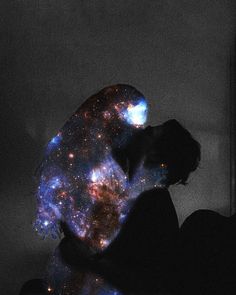 a person sitting in front of a window with their hands on their knees, looking at the stars