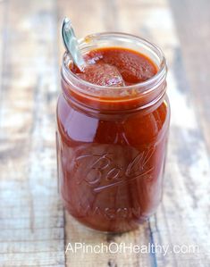 a jar filled with red sauce sitting on top of a wooden table next to a spoon