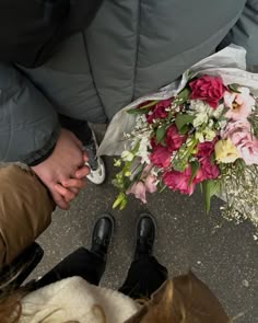 a bouquet of flowers is placed on the ground next to someone's feet and shoes