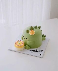 a green cake with an adorable little dinosaur on it's side and a cupcake next to it