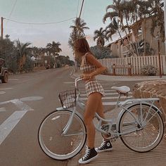 a woman standing next to a bike on the side of a road with palm trees in the background