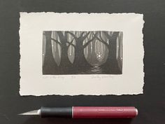 a red pen sitting next to a black and white photo with trees in the background