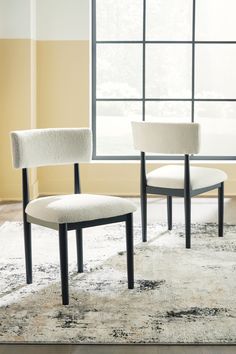 two white chairs sitting on top of a rug in front of a window with an area rug