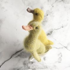 two knitted ducks sitting on top of a white bowl filled with something yellow and pink