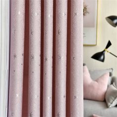 a living room with pink curtains and black lamps on the wall next to a gray couch