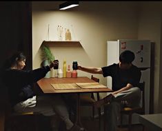 two people sitting at a table with drinks in front of them and one person reaching for something