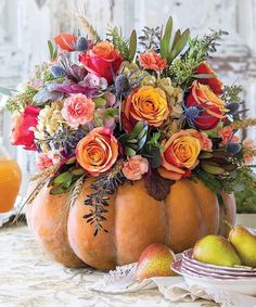 a pumpkin filled with lots of flowers sitting on top of a table next to fruit