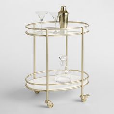 a gold bar cart with two glasses on top and one empty glass in the middle