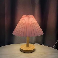 a pink lamp sitting on top of a wooden table next to a curtained wall