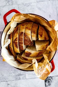 sliced bread in a red pot on a marble counter top with parchment paper around it