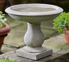 a cement planter sitting on top of a stone slab next to potted plants