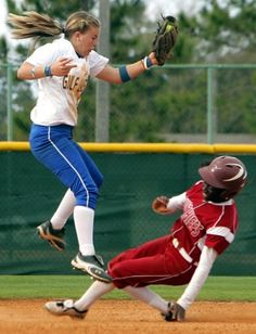 two girls playing baseball on a field with one trying to catch the ball while the other tries to slide into home plate